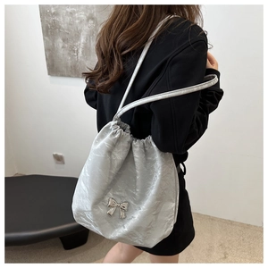 Detail of silver pleated tote bag with metal butterfly pendant and drawstring closure