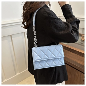 Detailed side view of a light blue quilted chain shoulder bag worn by a model in a room