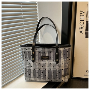 Detail of grey plaid tote bag with black 3D dots, leather handles and brand logo tag