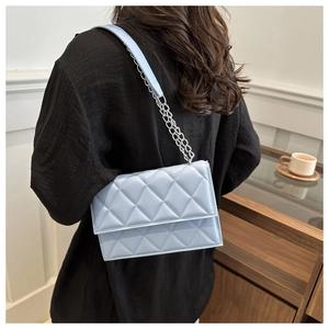 Detail of light blue quilted crossbody bag with silver chain strap shown on a model
