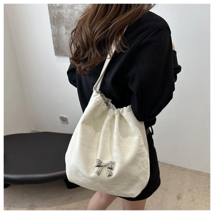 Detail of white drawstring bucket bag with shiny texture and silver metal bow ornament