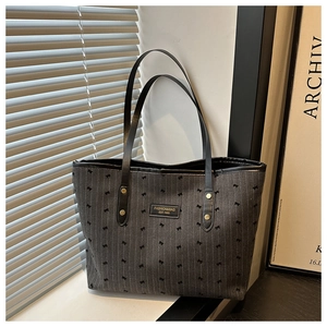 Close-up of dark grey tote bag featuring small bow patterns and a black leather logo patch