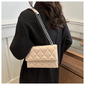 Detail of beige quilted shoulder bag with silver chain strap shown on model in a cafe