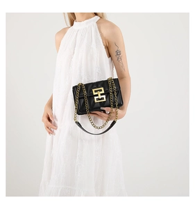 Détail du sac bandoulière noir matelassé avec chaîne dorée et fermoir sur robe blanche