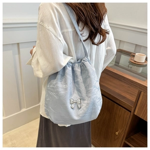 Détail du sac à cordon bleu clair en tissu froissé avec un nœud décoratif argenté
