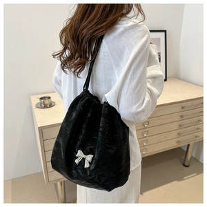 Détail du sac seau noir à cordon avec nœud argenté porté à l'épaule par un mannequin