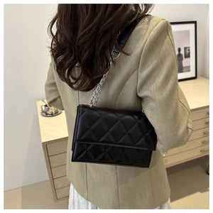 Close-up of a black quilted chain bag worn by a model in a minimalist interior setting