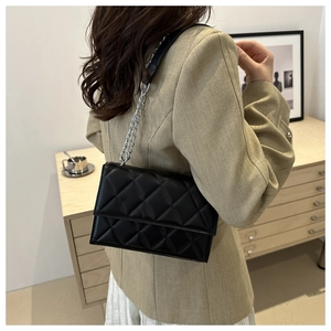 Detail of black quilted leather shoulder bag with silver chain strap on model