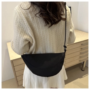 Bolso bandolera negro de media luna en una modelo que lleva un jersey de punto beige