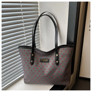 Detail of gray tote bag with red heart prints, black leather handles and gold rivet hardware
