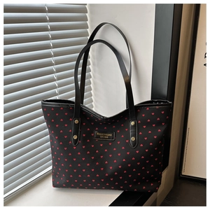 Detail of black canvas tote bag with red heart patterns and branded leather logo patch