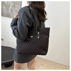 Model side view of black tote bag with red heart pattern and adjustable shoulder strap