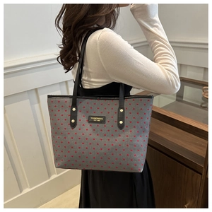 Detail of grey fabric tote bag with red heart pattern and gold studded black straps