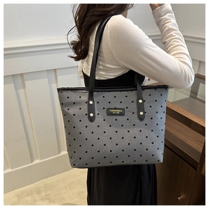 Detailed view of gray polka dot tote bag with leather handles and metallic logo plate