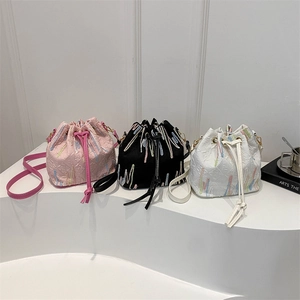 Three embroidered drawstring bucket bags in pink, black, and white on a display stand