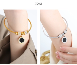 Detail of steel cable bangles with zirconia-studded black enamel round charms in gold and silver