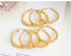Gros plan de boucles d'oreilles créoles dorées texturées avec motif tissé sur un magazine