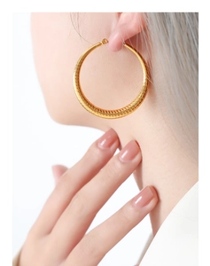 Gros plan de grandes boucles d'oreilles créoles dorées texturées sur modèle