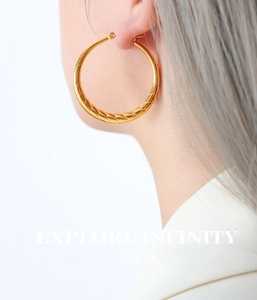 Détail macro de grandes créoles dorées torsadées portées par un mannequin chic
