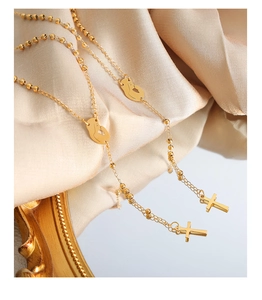 Detail of gold layered bead chain with cross pendant and silhouette charm on silk