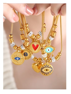 Detalle de pulsera de cadena de serpiente dorada con dijes de ojo y corazón rojo