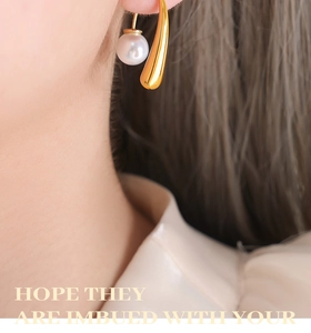 Gros plan de boucles d'oreilles pendantes dorées avec perle ronde sur une oreille