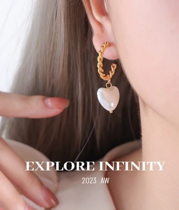 Détail d'une boucle d'oreille dorée torsadée avec pendentif perle cœur sur un mannequin