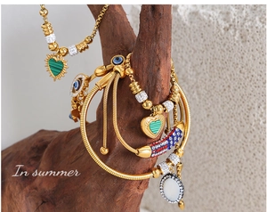 Detail of bohemian gold bracelet with green enamel heart and evil eye charm on wood