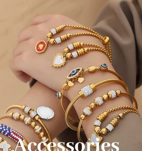 Detail of stacked gold bracelets featuring blue evil eye and heart charms on model wrist