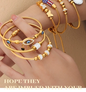 Stacked golden steel cable bracelets with evil eye charms and butterfly pendants