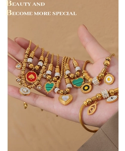 Detailed view of gold snake chain bracelets with heart and evil eye charms on a model