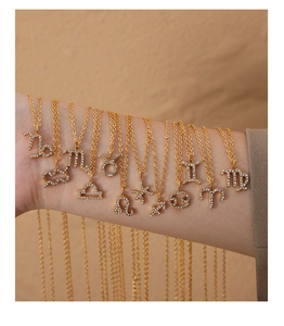 Detail view of twelve gold zodiac necklaces with sparkling rhinestones worn on an arm