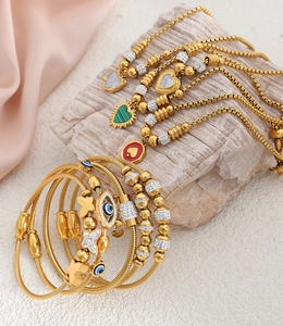 Detail of gold jewelry set featuring heart pendants and evil eye beaded bracelet charms