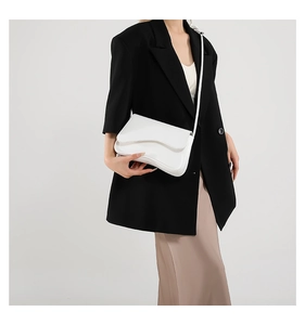Minimalist white leather crossbody bag detail with elegant curved flap on black blazer