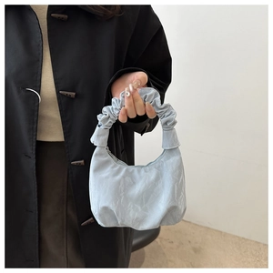 Détail d'un sac bleu clair avec poignée plissée et texture de surface sur fond de manteau noir