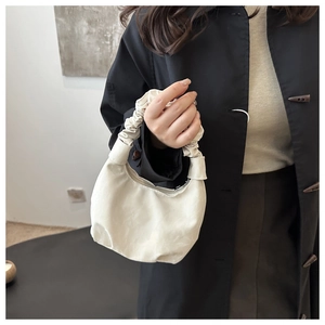 Mannequin portant un sac à main beige à anse plissée nuage avec un trench-coat noir