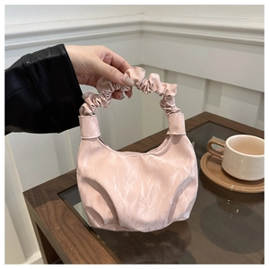 Détail d'un sac à main en satin plissé rose clair avec une anse froncée et zip en métal