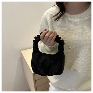 Détail d'un sac à main noir avec poignée froncée et texture élégante en tissu plissé