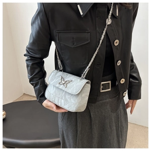 Close-up of a silver textured crossbody bag with a butterfly metal buckle on leather jacket
