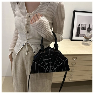 Gothic black crossbody bag with white spider web stitching on a minimalist wooden cabinet