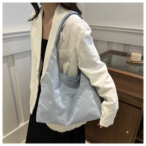 Detail of light blue wrinkled tote bag featuring a metallic triangle logo on textured fabric