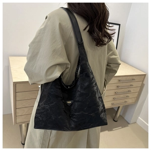 Dettaglio di una borsa shopper nera con logo triangolare metallico e finitura pieghettata