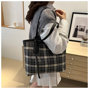 Detail of checkered tote bag with black leather straps and stylish hanging pendant