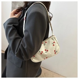 Detail of white corduroy underarm bag featuring red cherry print and matching strap