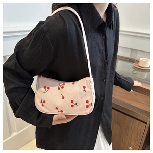 Close-up of pink corduroy shoulder bag with detailed red cherry embroidery on a model