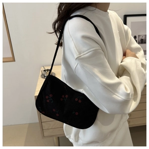 Detail of black corduroy shoulder bag with red cherry embroidery and elegant single strap