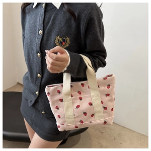 Detail of pink corduroy tote bag featuring red strawberry prints and cream handles