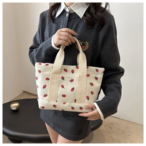 Detail of white corduroy tote bag featuring red strawberry patterns and woven handles