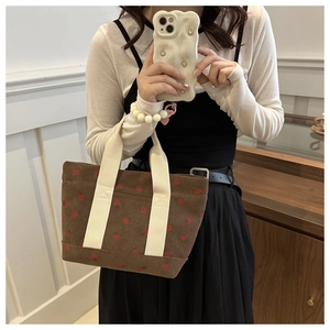 Detail of dark brown corduroy tote bag with red strawberry patterns and beige handles
