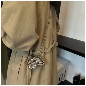 Detail of a silver snail-shaped shell evening bag with metal chain on a khaki trench coat